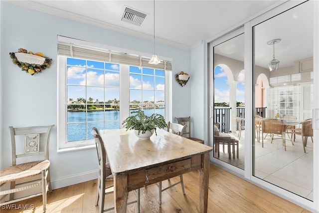 dining space with a water view, crown molding, a healthy amount of sunlight, and light wood-type flooring