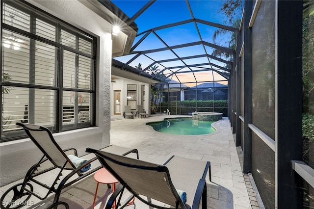 pool at dusk with glass enclosure and a patio area