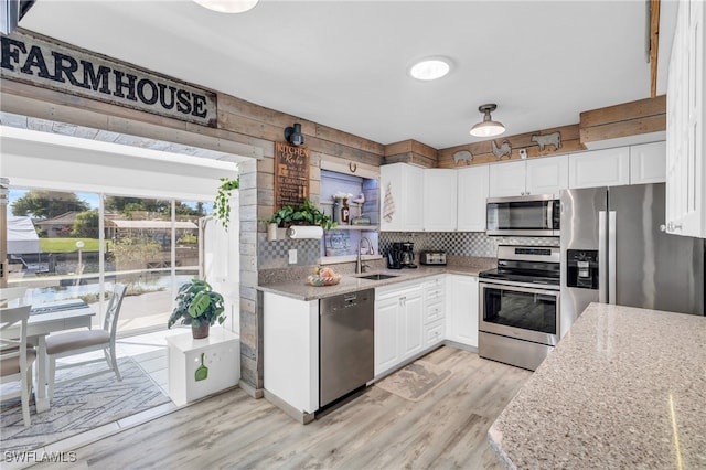 kitchen with light hardwood / wood-style floors, stainless steel appliances, light stone counters, and white cabinets