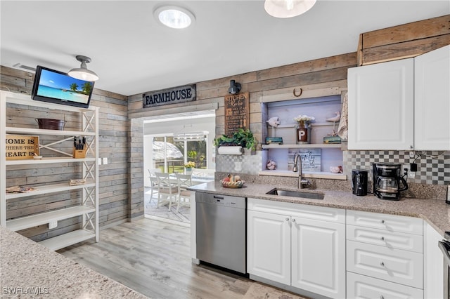 kitchen with white cabinets, stainless steel dishwasher, wooden walls, light hardwood / wood-style floors, and sink