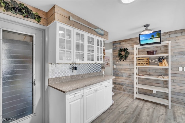 kitchen featuring white cabinetry, tasteful backsplash, light hardwood / wood-style flooring, and wooden walls