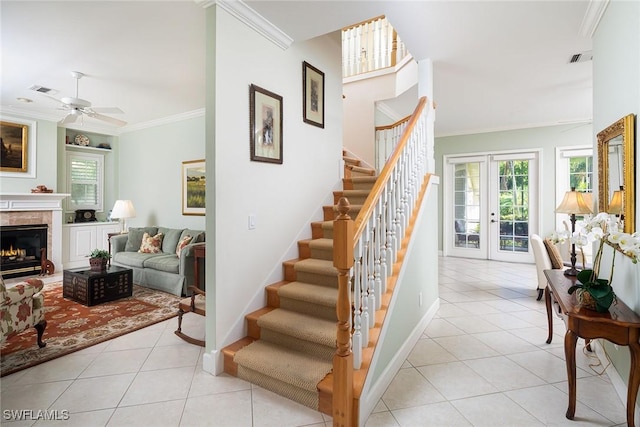 staircase with a warm lit fireplace, tile patterned flooring, baseboards, french doors, and ornamental molding