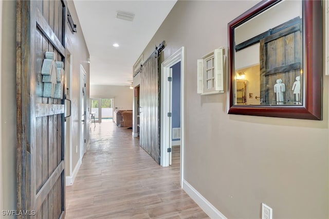 hallway with a barn door and light hardwood / wood-style flooring