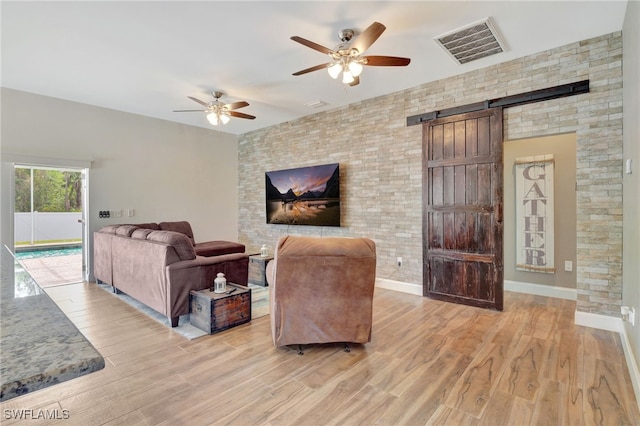 living room featuring ceiling fan, a barn door, and light hardwood / wood-style flooring