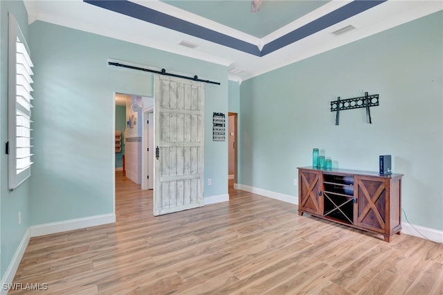 spare room featuring a barn door, light hardwood / wood-style flooring, and crown molding