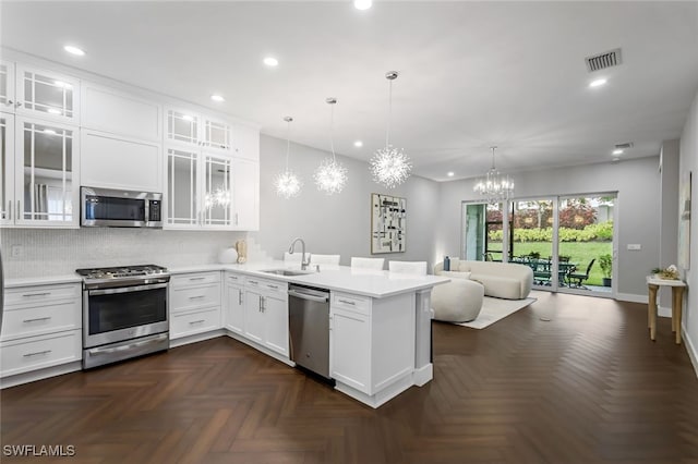 kitchen with stainless steel appliances, light countertops, glass insert cabinets, and decorative light fixtures