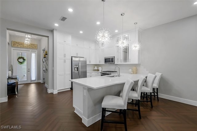 kitchen with dark parquet flooring, white cabinets, appliances with stainless steel finishes, decorative light fixtures, and kitchen peninsula