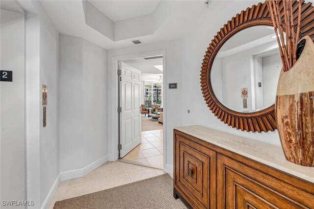 corridor featuring light tile patterned floors, visible vents, a tray ceiling, and baseboards