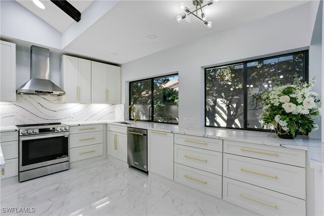 kitchen featuring lofted ceiling, appliances with stainless steel finishes, white cabinets, decorative backsplash, and wall chimney exhaust hood