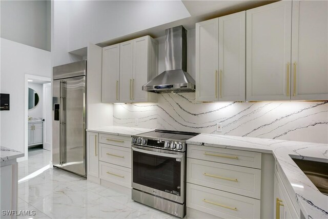 kitchen with stainless steel appliances, white cabinetry, light stone countertops, and wall chimney range hood