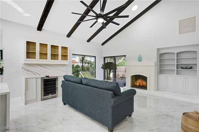 living room with ceiling fan, high vaulted ceiling, a brick fireplace, beverage cooler, and beamed ceiling