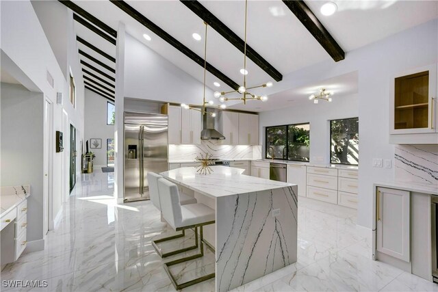 kitchen with appliances with stainless steel finishes, white cabinetry, a kitchen island, decorative backsplash, and beamed ceiling