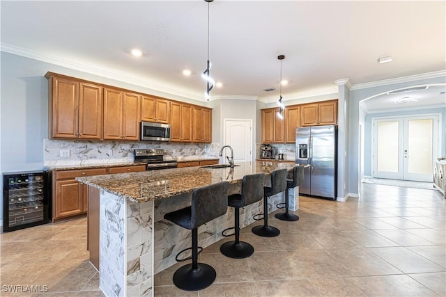 kitchen with stainless steel appliances, french doors, an island with sink, beverage cooler, and hanging light fixtures