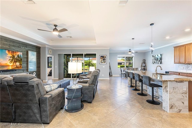 tiled living room with ceiling fan, crown molding, a raised ceiling, and sink