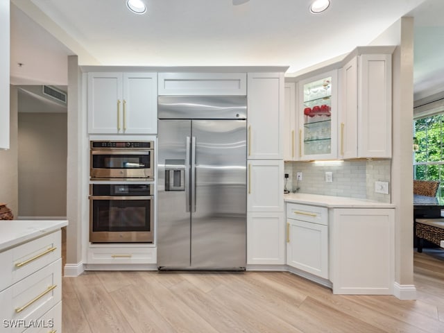 kitchen featuring white cabinets, stainless steel appliances, light hardwood / wood-style flooring, and tasteful backsplash