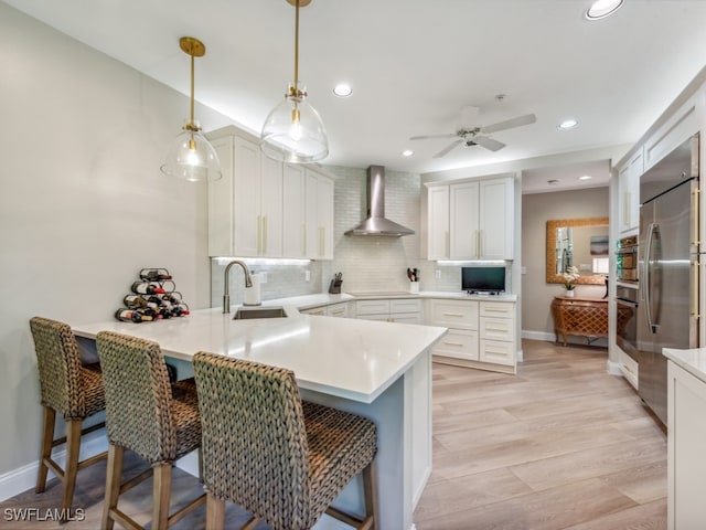 kitchen featuring white cabinetry, sink, wall chimney exhaust hood, kitchen peninsula, and a breakfast bar area