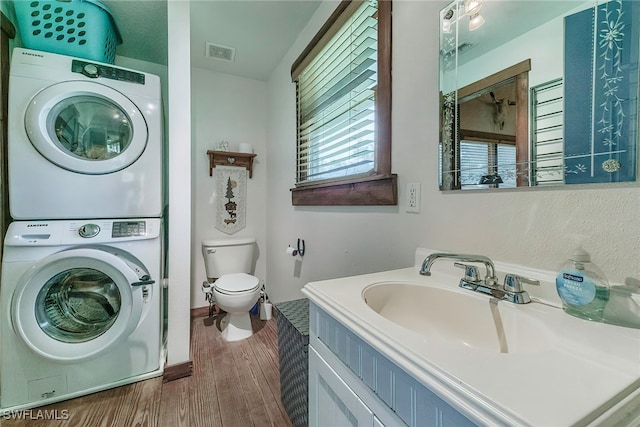 bathroom with wood-type flooring, toilet, vanity, and stacked washer and dryer