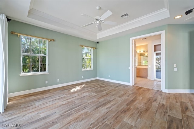 empty room featuring a tray ceiling, light hardwood / wood-style flooring, a wealth of natural light, and ornamental molding