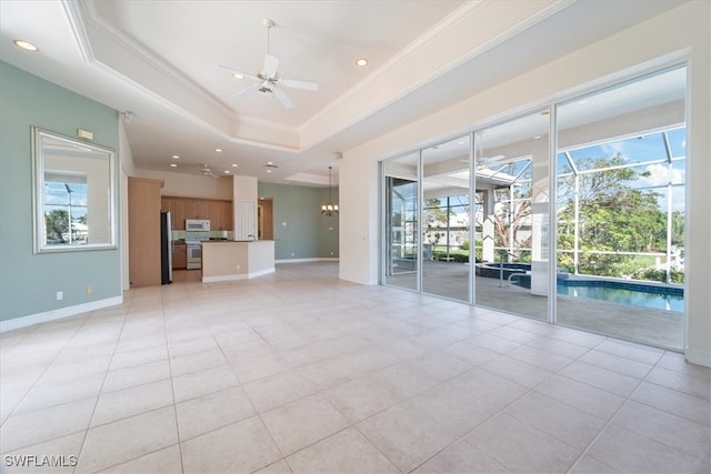 unfurnished living room featuring ceiling fan with notable chandelier, a healthy amount of sunlight, a raised ceiling, and light tile patterned floors