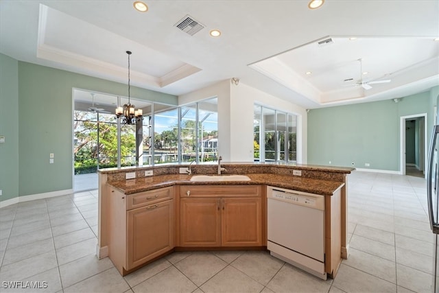 kitchen with a tray ceiling, a kitchen island with sink, dishwasher, and sink