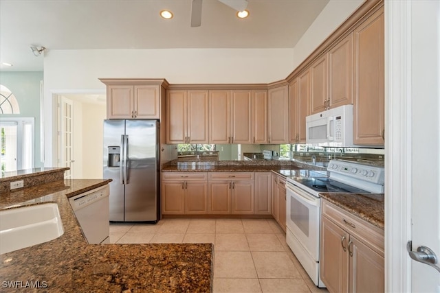 kitchen featuring light brown cabinetry, white appliances, light tile patterned floors, and dark stone countertops