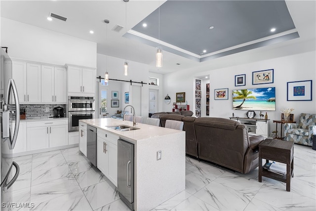 kitchen with an island with sink, white cabinetry, a barn door, and sink