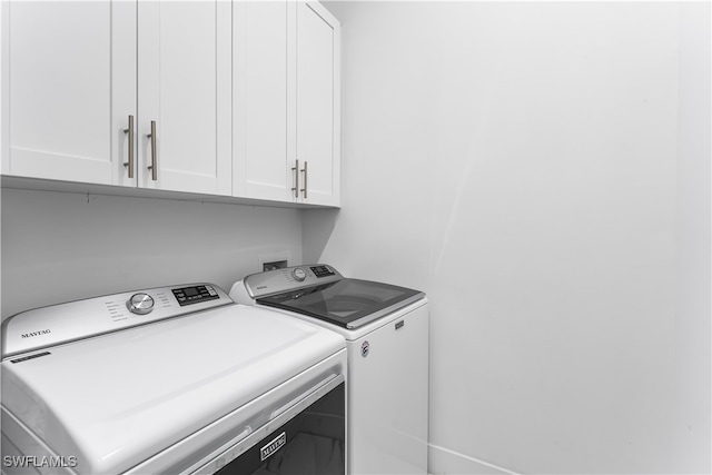 clothes washing area featuring washing machine and clothes dryer and cabinets