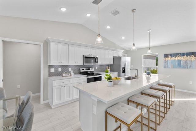 kitchen featuring hanging light fixtures, a center island with sink, white cabinetry, appliances with stainless steel finishes, and vaulted ceiling