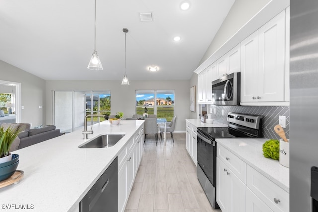 kitchen with appliances with stainless steel finishes, decorative light fixtures, white cabinetry, lofted ceiling, and sink