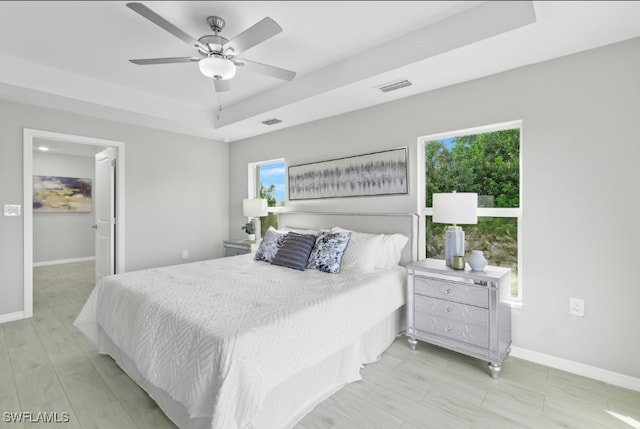 bedroom featuring a raised ceiling, a spacious closet, ceiling fan, and light hardwood / wood-style flooring