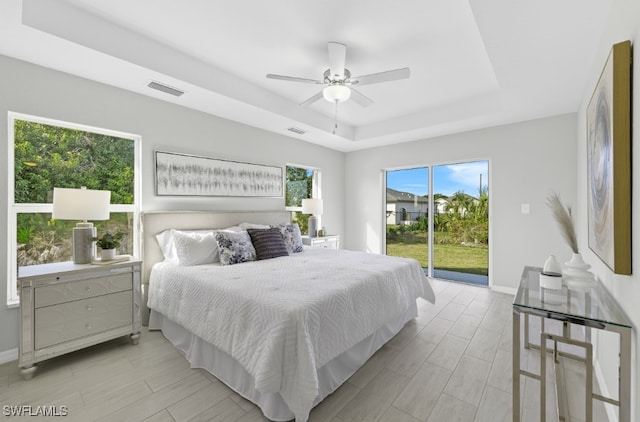 bedroom with ceiling fan, a tray ceiling, and access to exterior