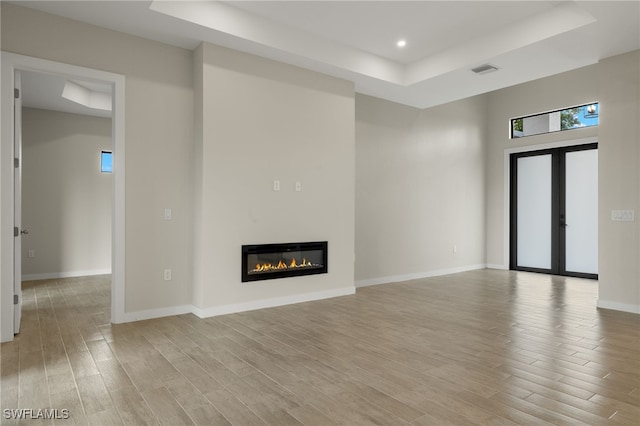 unfurnished living room with visible vents, a raised ceiling, a glass covered fireplace, recessed lighting, and light wood-style flooring