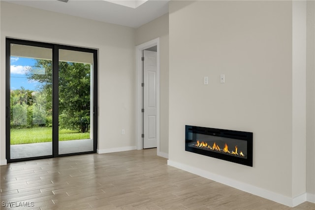 unfurnished living room with baseboards, a glass covered fireplace, and wood finished floors