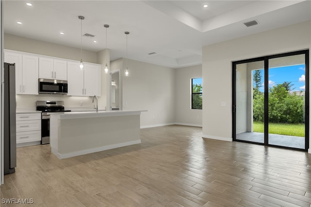 kitchen with white cabinetry, stainless steel appliances, hanging light fixtures, and an island with sink