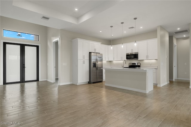 kitchen with white cabinets, hanging light fixtures, appliances with stainless steel finishes, a kitchen island with sink, and light hardwood / wood-style floors