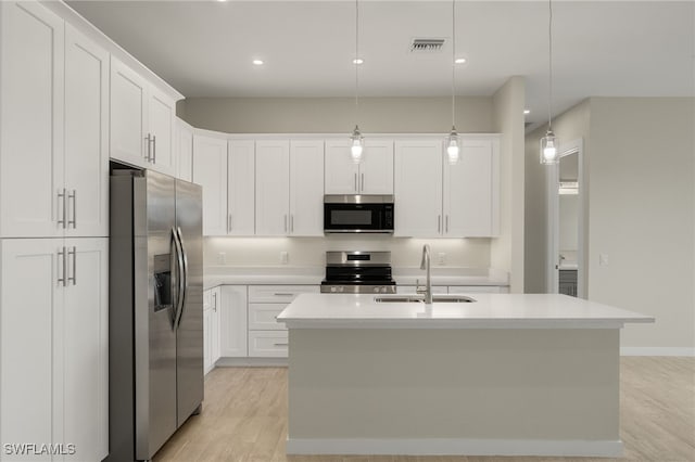 kitchen featuring appliances with stainless steel finishes, a center island with sink, sink, and hanging light fixtures