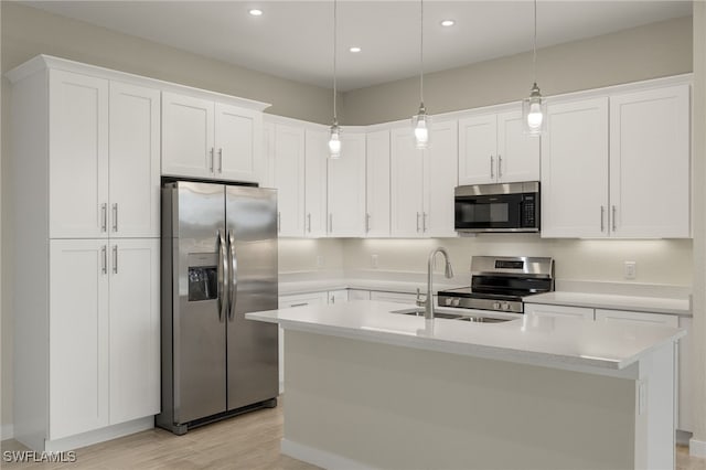 kitchen with sink, hanging light fixtures, white cabinetry, stainless steel appliances, and a center island with sink