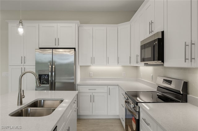 kitchen with white cabinets, a sink, light wood-style flooring, stainless steel appliances, and decorative light fixtures