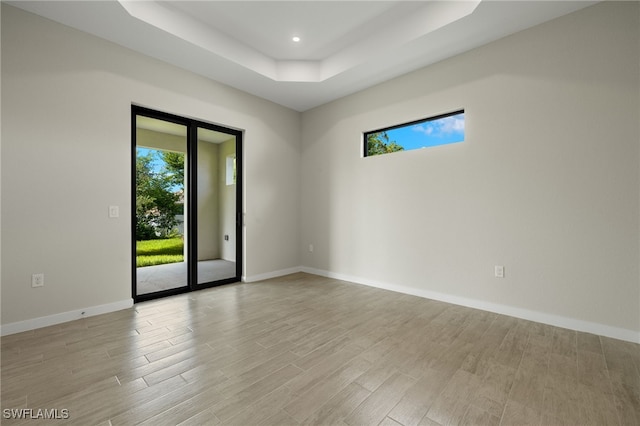 spare room with a tray ceiling and light wood-type flooring