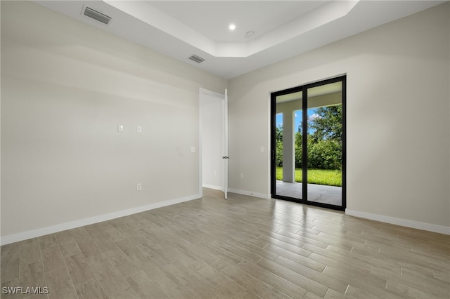 spare room featuring baseboards, visible vents, light wood finished floors, and a raised ceiling