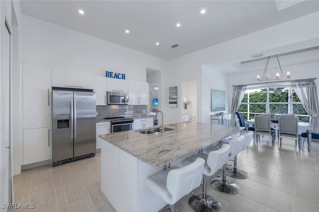 kitchen featuring stainless steel appliances, a sink, white cabinetry, a breakfast bar area, and light stone counters
