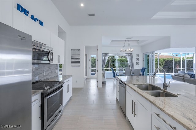 kitchen with stainless steel appliances, a tray ceiling, a sink, decorative backsplash, and white cabinets
