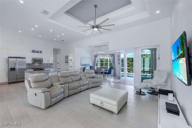 living area with a high ceiling, recessed lighting, a ceiling fan, and a raised ceiling