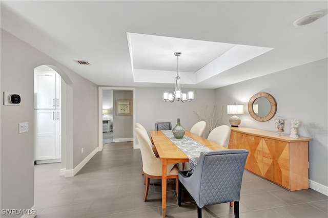 tiled dining room featuring a raised ceiling and a notable chandelier