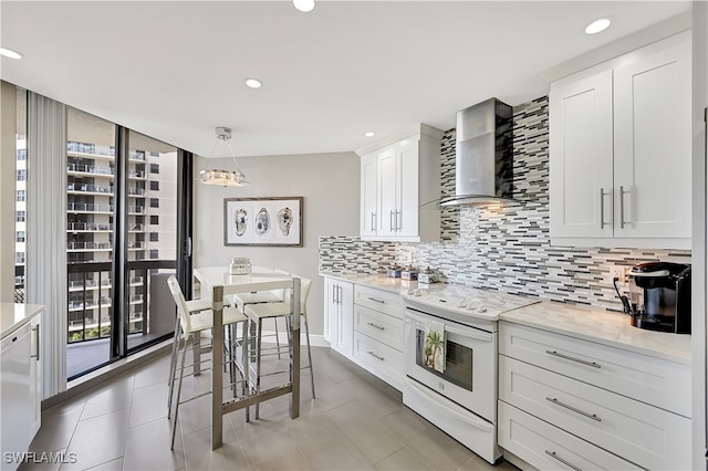 kitchen featuring a wealth of natural light, wall chimney exhaust hood, white cabinets, and white range with electric stovetop