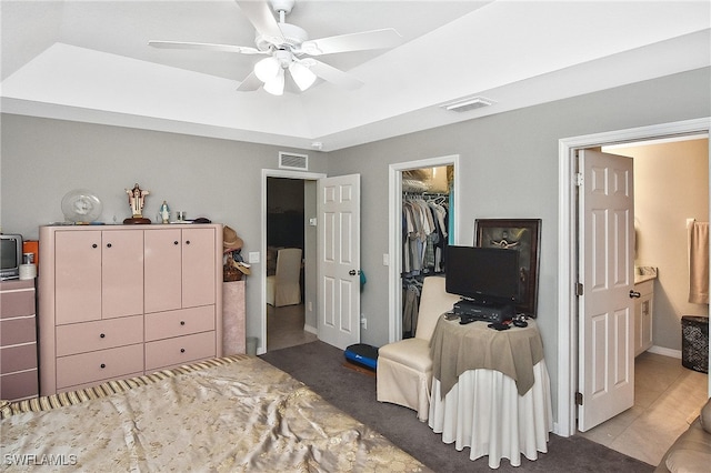 bedroom with a raised ceiling, a walk in closet, a closet, and ceiling fan