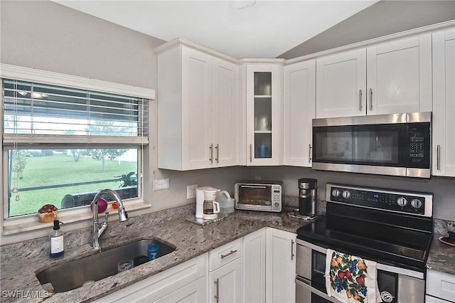 kitchen with appliances with stainless steel finishes, white cabinetry, sink, and vaulted ceiling