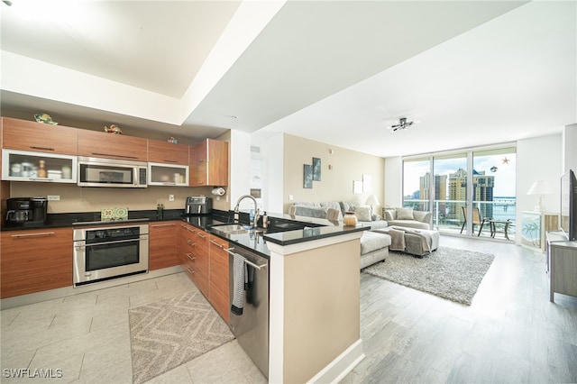 kitchen featuring expansive windows, sink, kitchen peninsula, light hardwood / wood-style flooring, and appliances with stainless steel finishes