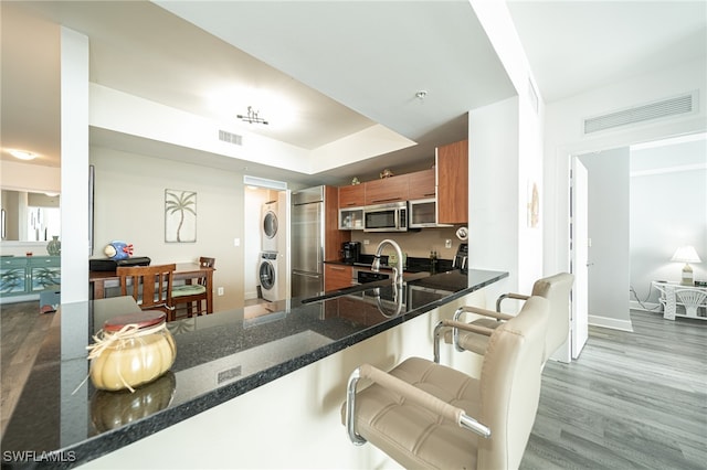 kitchen featuring hardwood / wood-style floors, stainless steel appliances, kitchen peninsula, a breakfast bar area, and stacked washer / drying machine