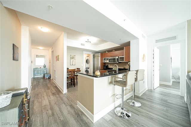 kitchen with stainless steel appliances, kitchen peninsula, light hardwood / wood-style flooring, stacked washer and clothes dryer, and a kitchen bar